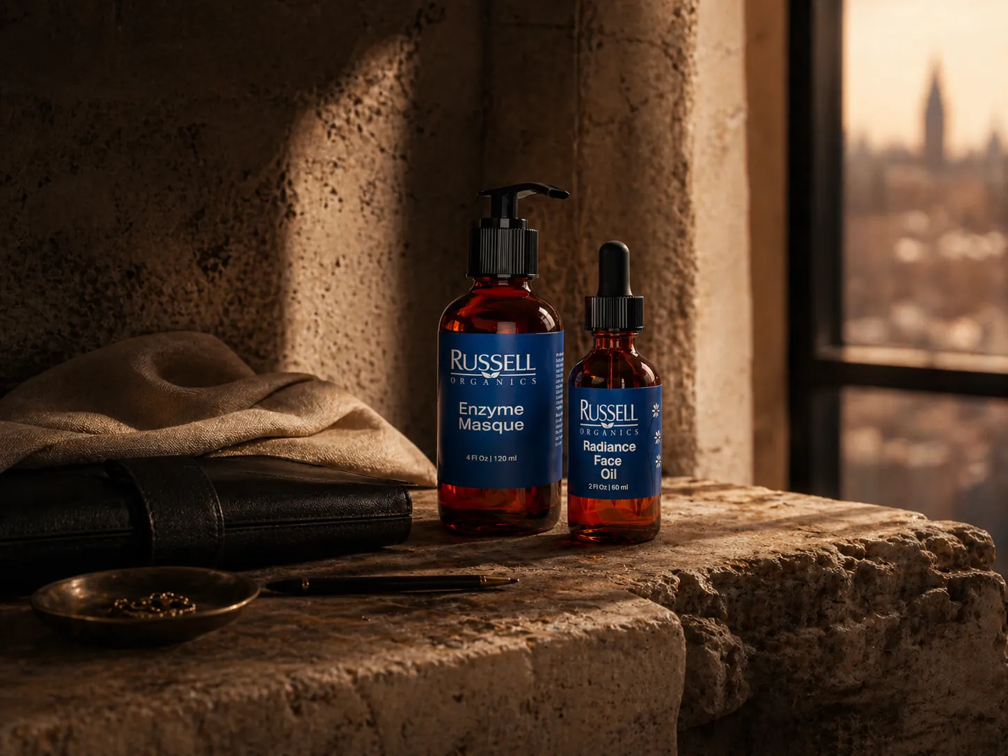 Russell Organics Enzyme Masque and Radiance Face Oil bottles on a stone ledge beside a cloth, a notebook and a window onto the city