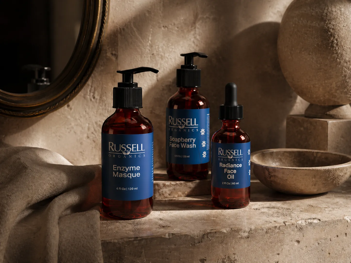 Three Russell Organics bottles — Enzyme Masque, Soapberry Face Wash and Radiance Face Oil — beside a stone bowl